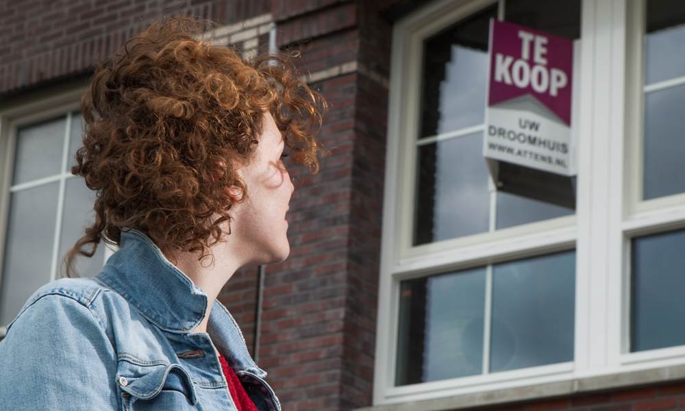 Vrouw kijkt naar tekoop bord op raam